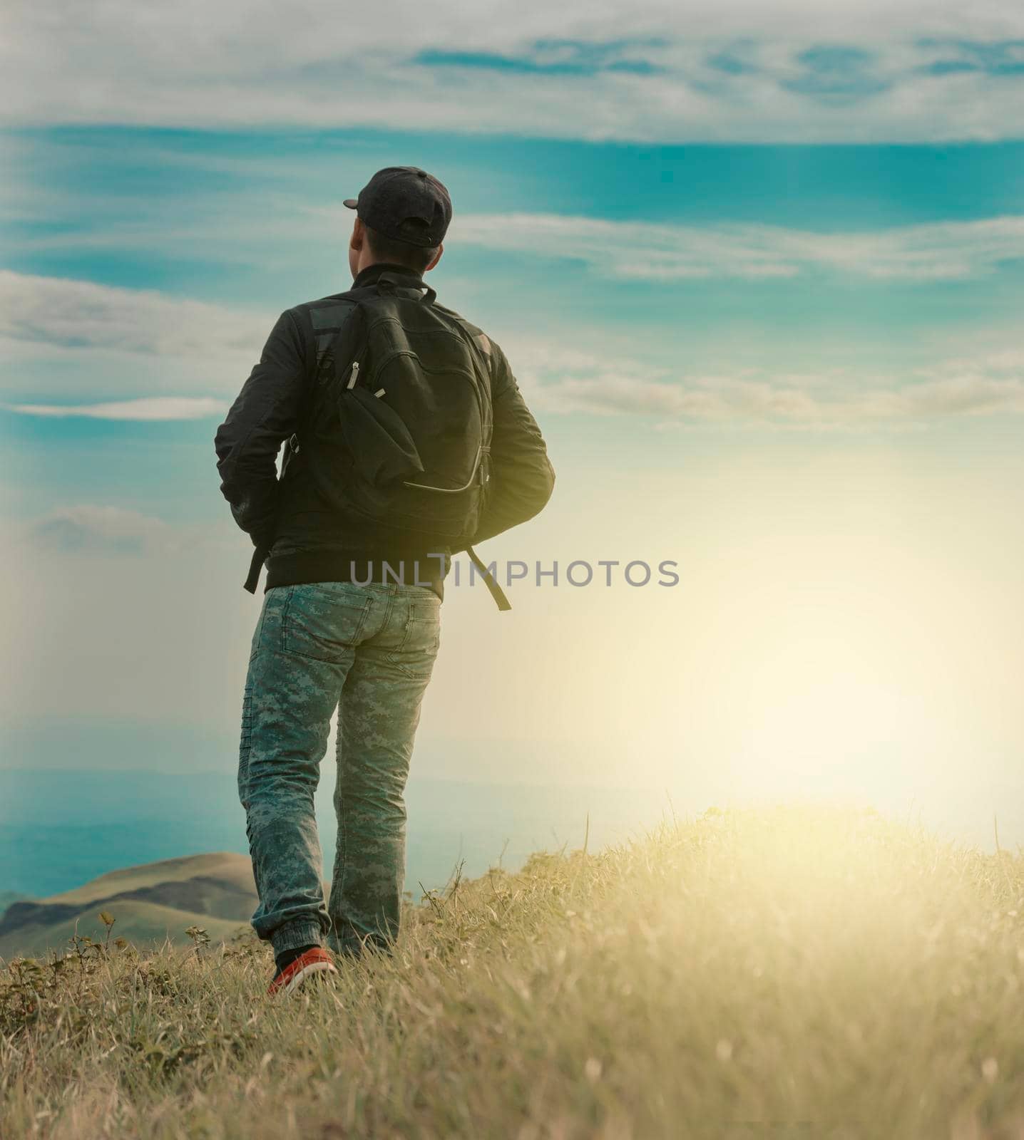 Backpacker man walking in field back view, close up of man from behind in field, low angle of backpacking man with copy space by isaiphoto