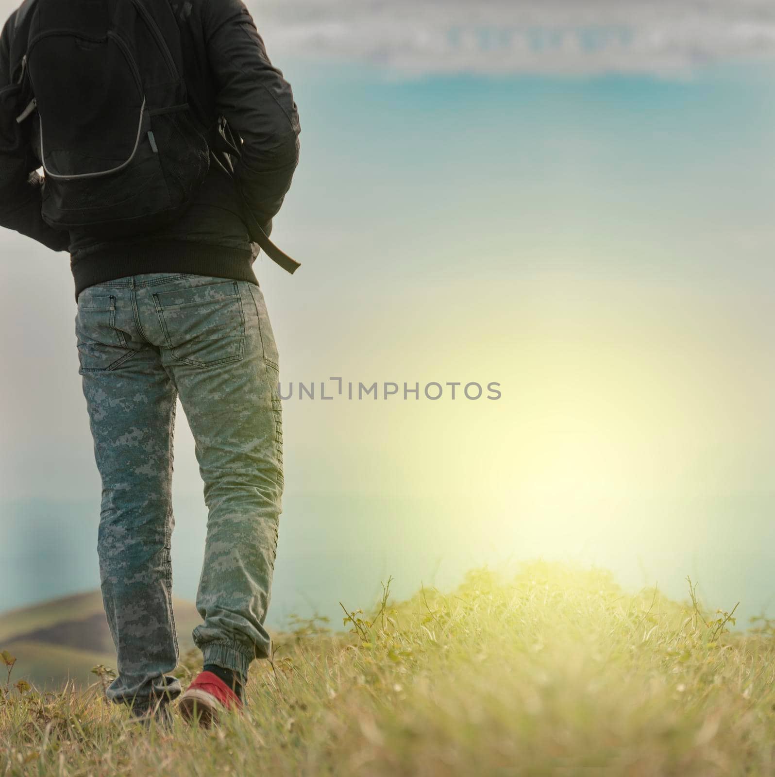 Backpacker man walking in field back view, close up of man from behind in field, low angle of backpacking man with copy space
