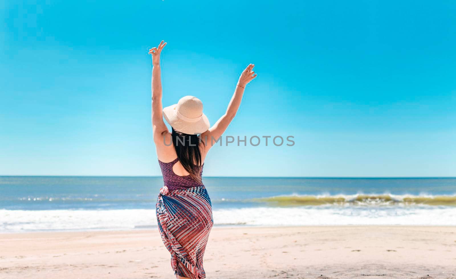 woman with hat from back on the beach, young woman raising her hands on the beach