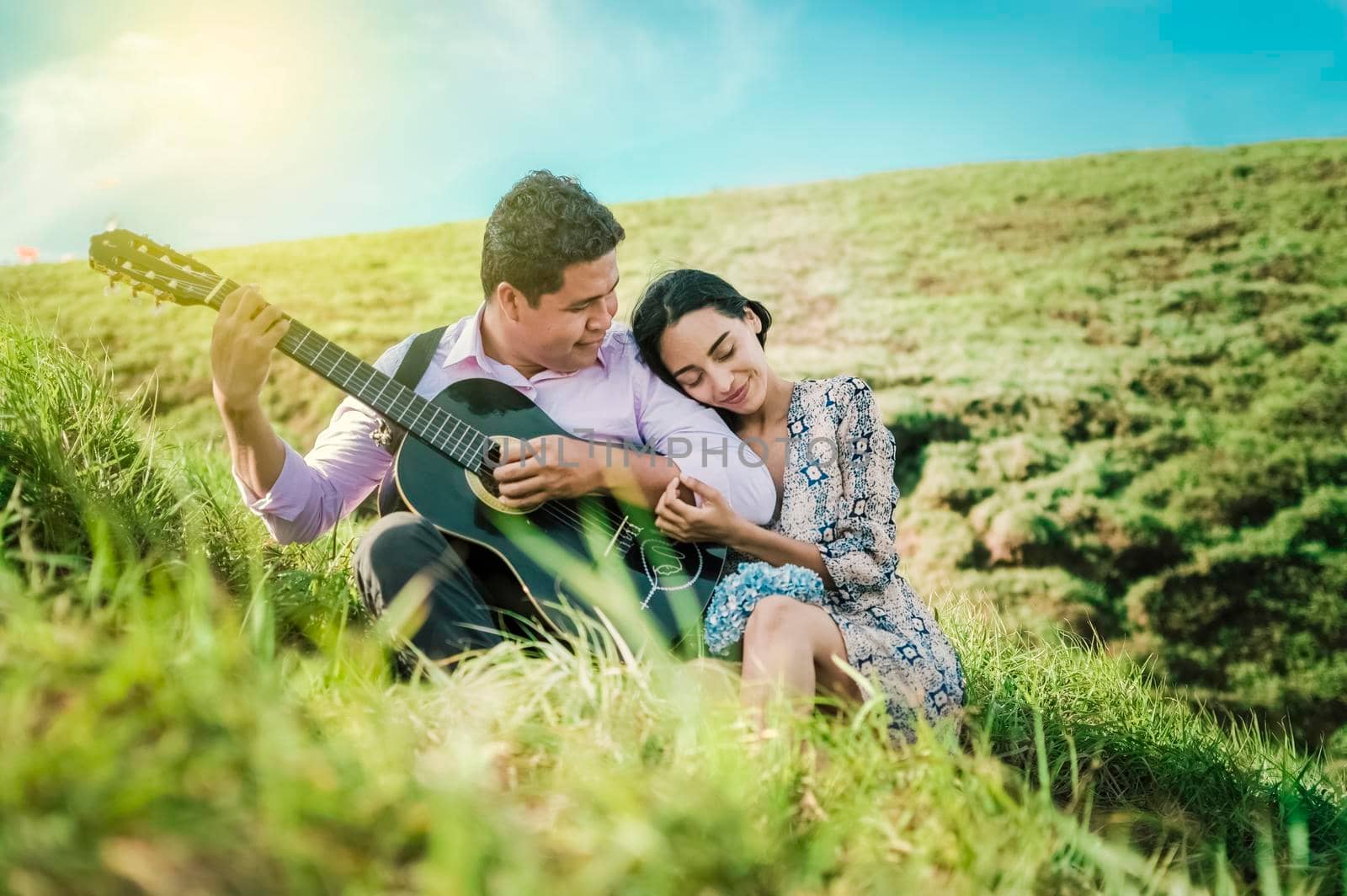 Man playing guitar to a girl, A woman leaning on the shoulder of a young man, man with woman in the field playing guitar