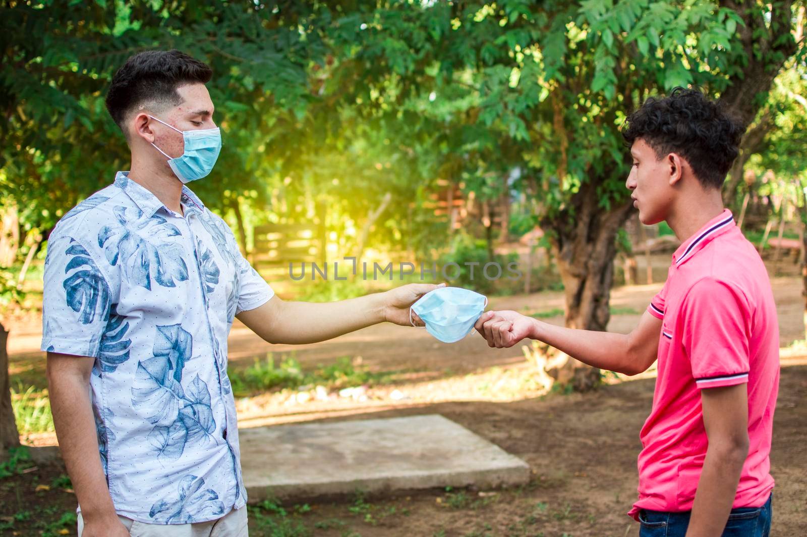 Two young people giving each other a mask, image of a young man giving a mask to another person, concept of a person offering a mask by isaiphoto