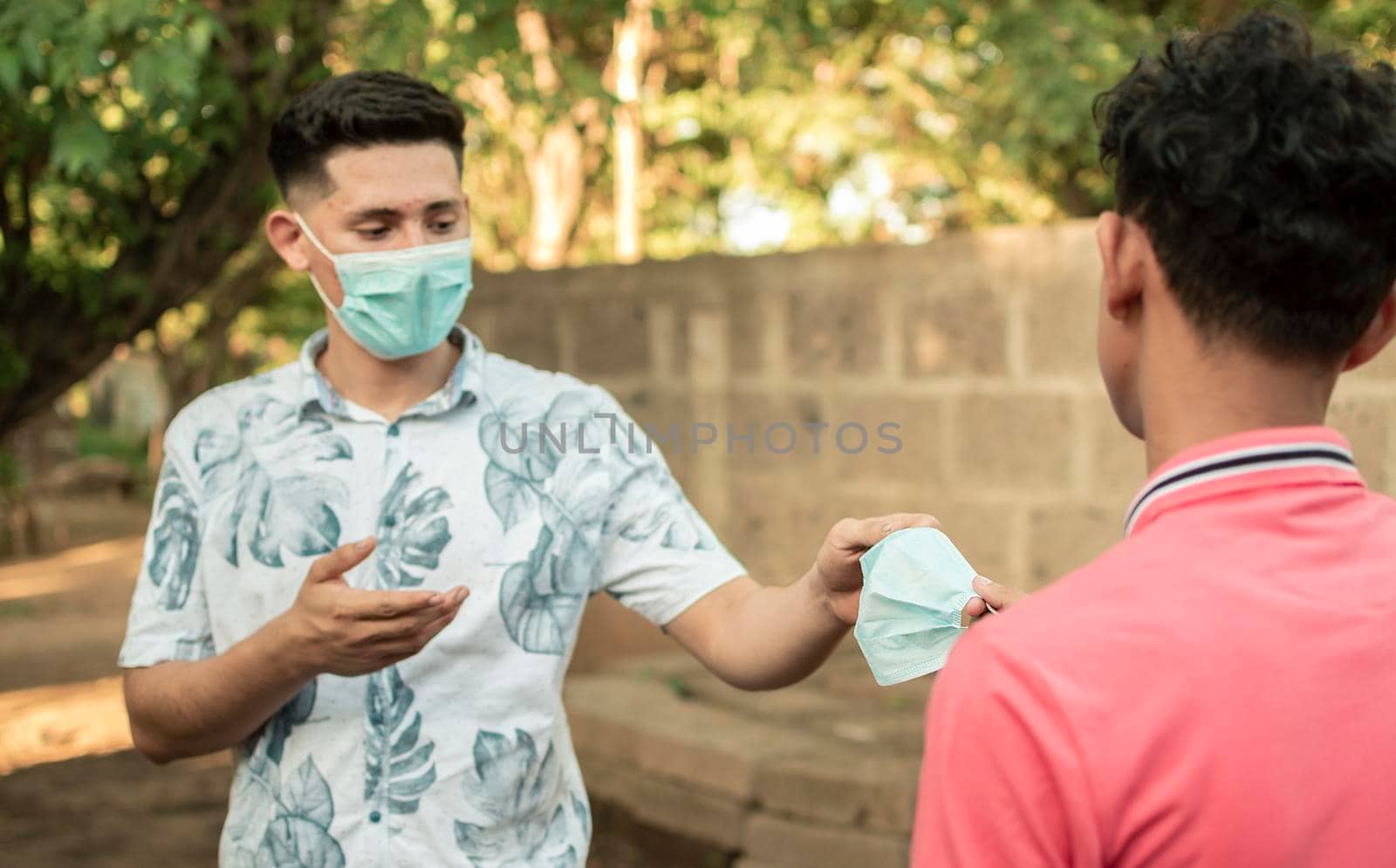 young man sharing mask to another young man, young man giving a mask to another young man, concept of giving a mask, by isaiphoto