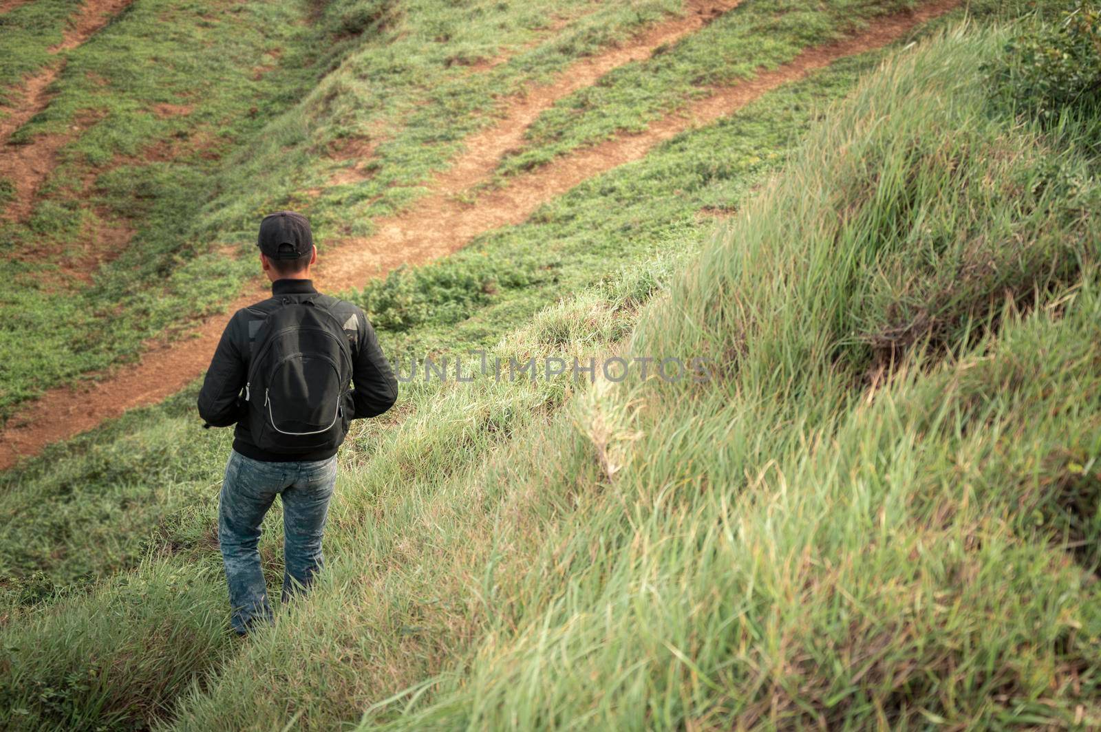 Backpacker man walking in the countryside, adventurous man descending from a hill, man with backpack going down a hill by isaiphoto