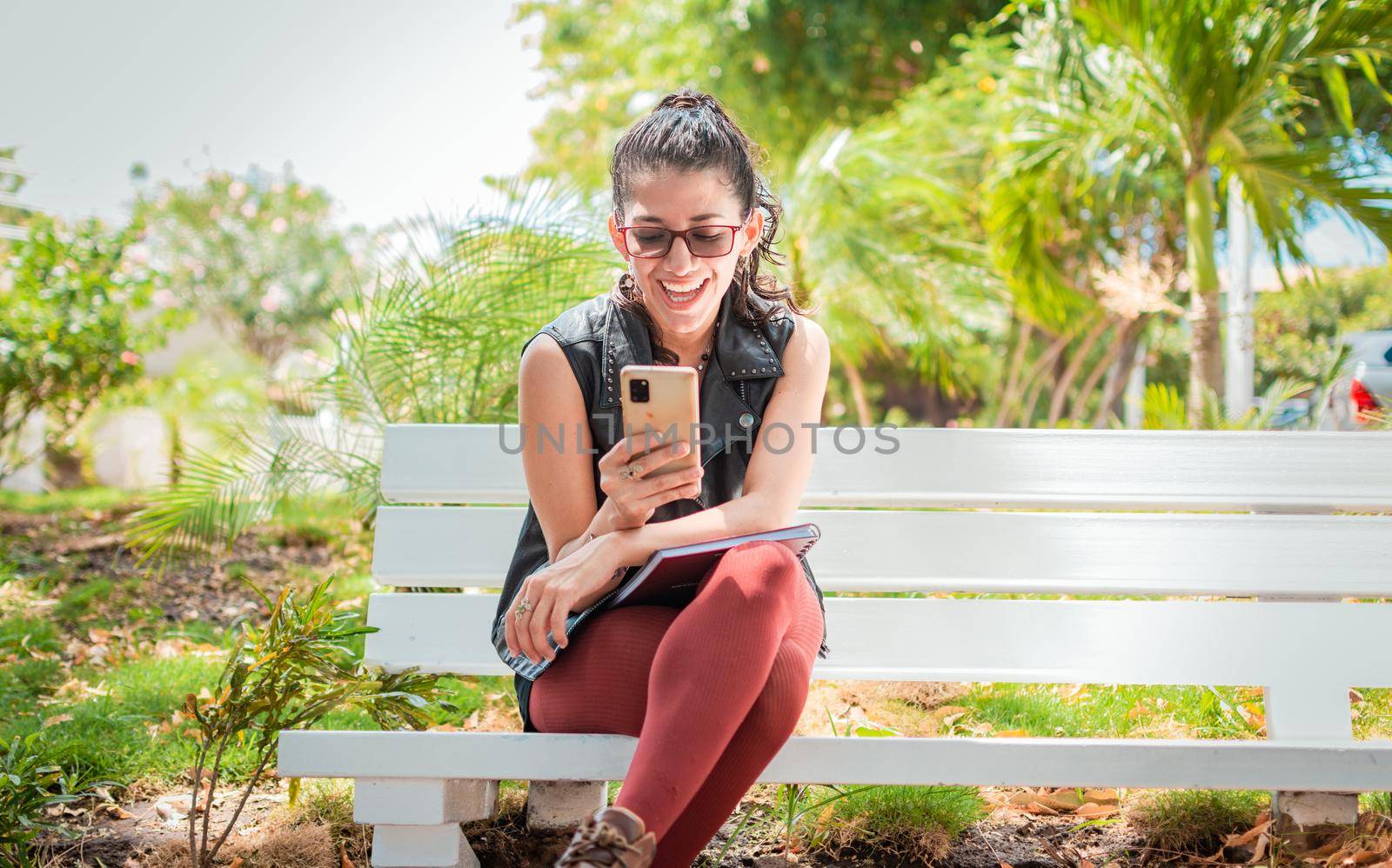 Girl sitting on a bench checking her cell phone, Happy woman sitting in a park texting on her cell phone, Woman sitting on a bench sending a text message