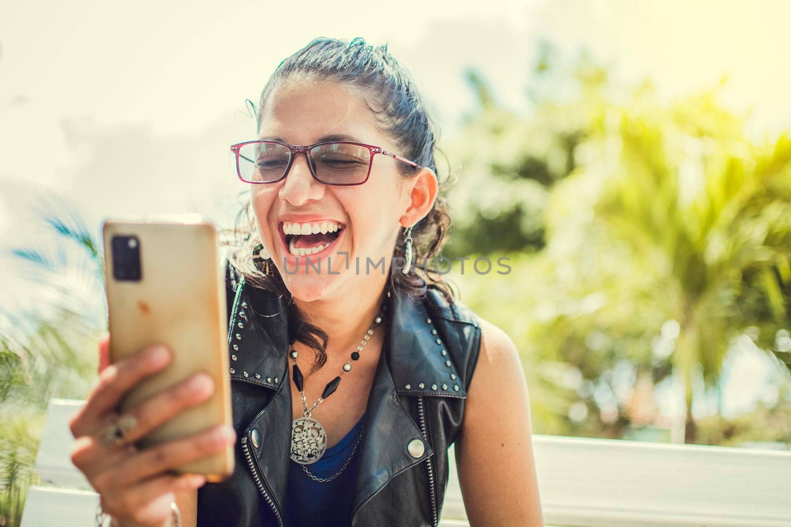 Close up of a happy girl checking her cell phone, Happy woman sitting with her cell phone outside, cell phone, Happy woman sitting on a bench sending a text message