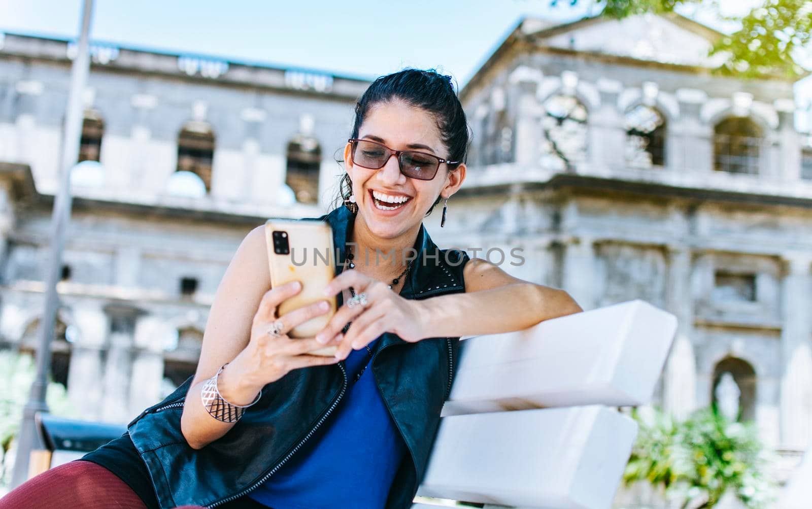 An attractive girl sitting on the cell phone smiling, Girl sitting on a bench texting on her cell phone, Urban style girl sitting on a bench with her cell phone by isaiphoto