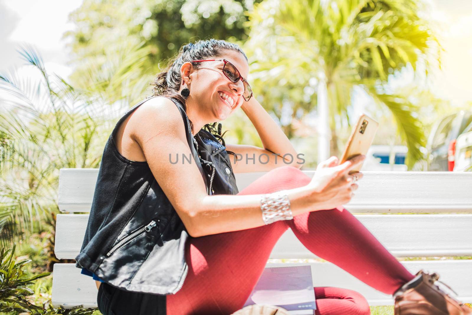 Girl sitting on a bench checking her cell phone, Happy woman sitting in a park texting on her cell phone, Happy woman sitting on a bench sending a text message