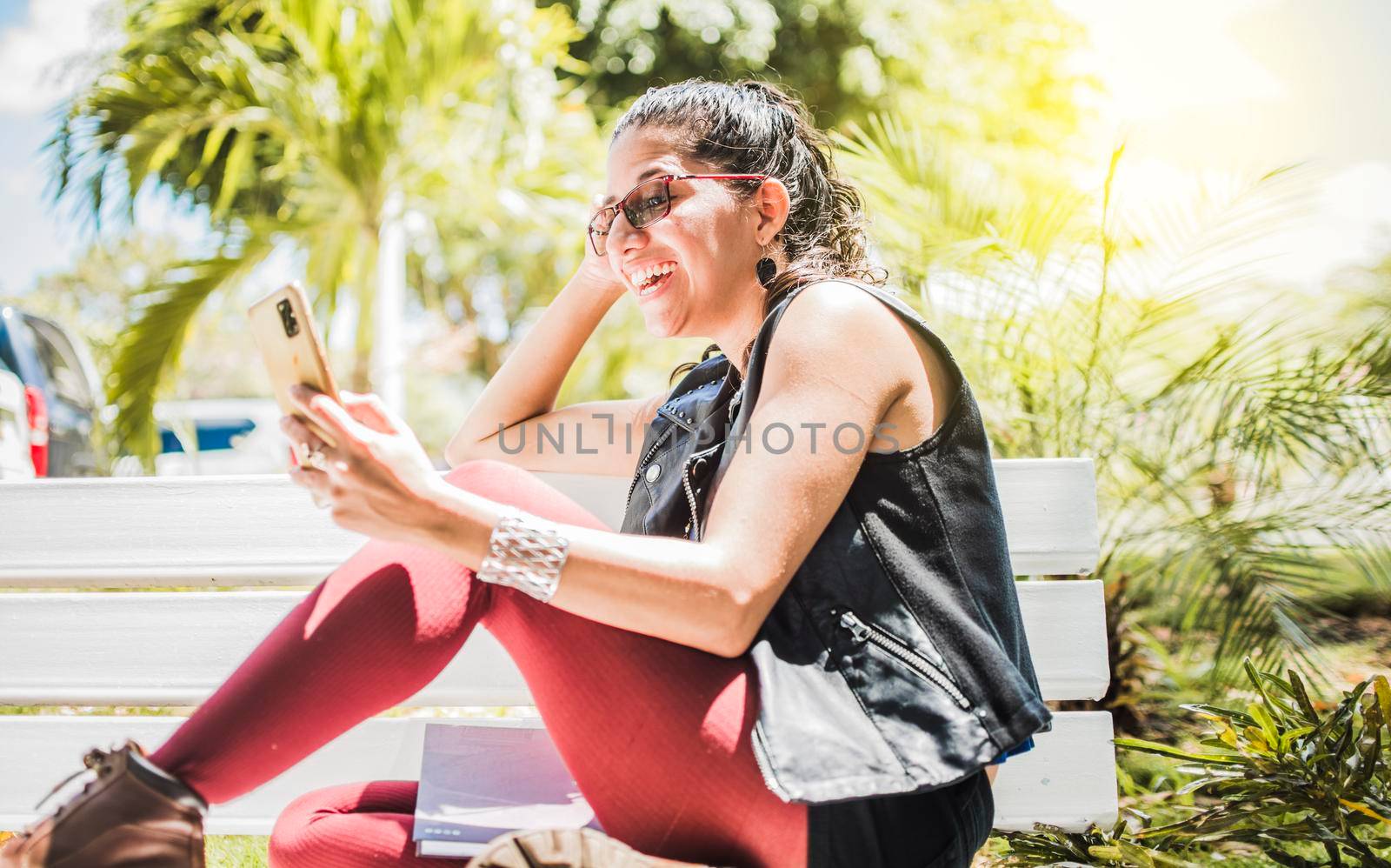 Girl sitting on a bench checking her cell phone, Happy woman sitting in a park texting on her cell phone, Happy woman sitting on a bench sending a text message