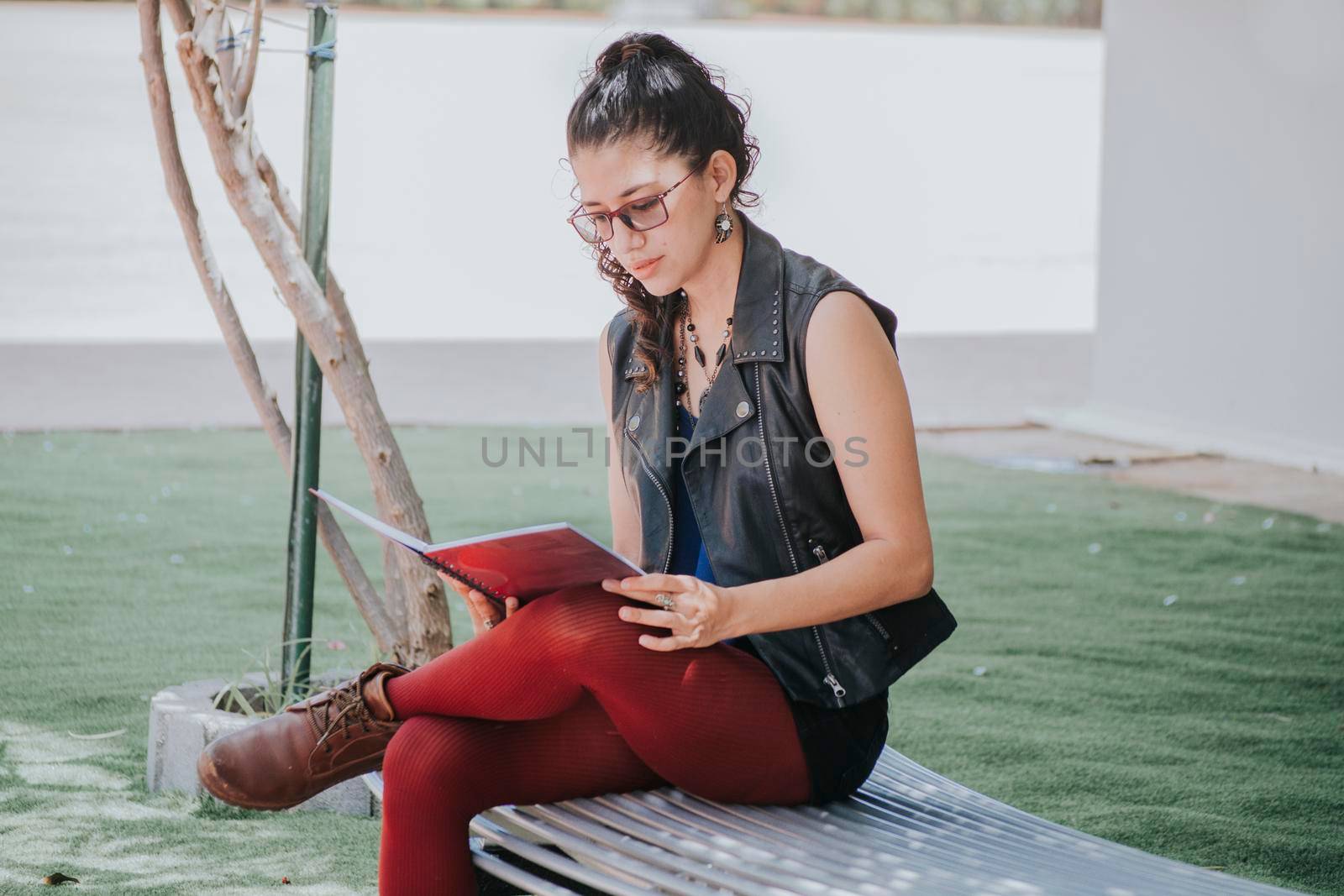 Urban girl sitting on a bench reading a book, Latin girl reading a book outside, concept of a student girl reading a book