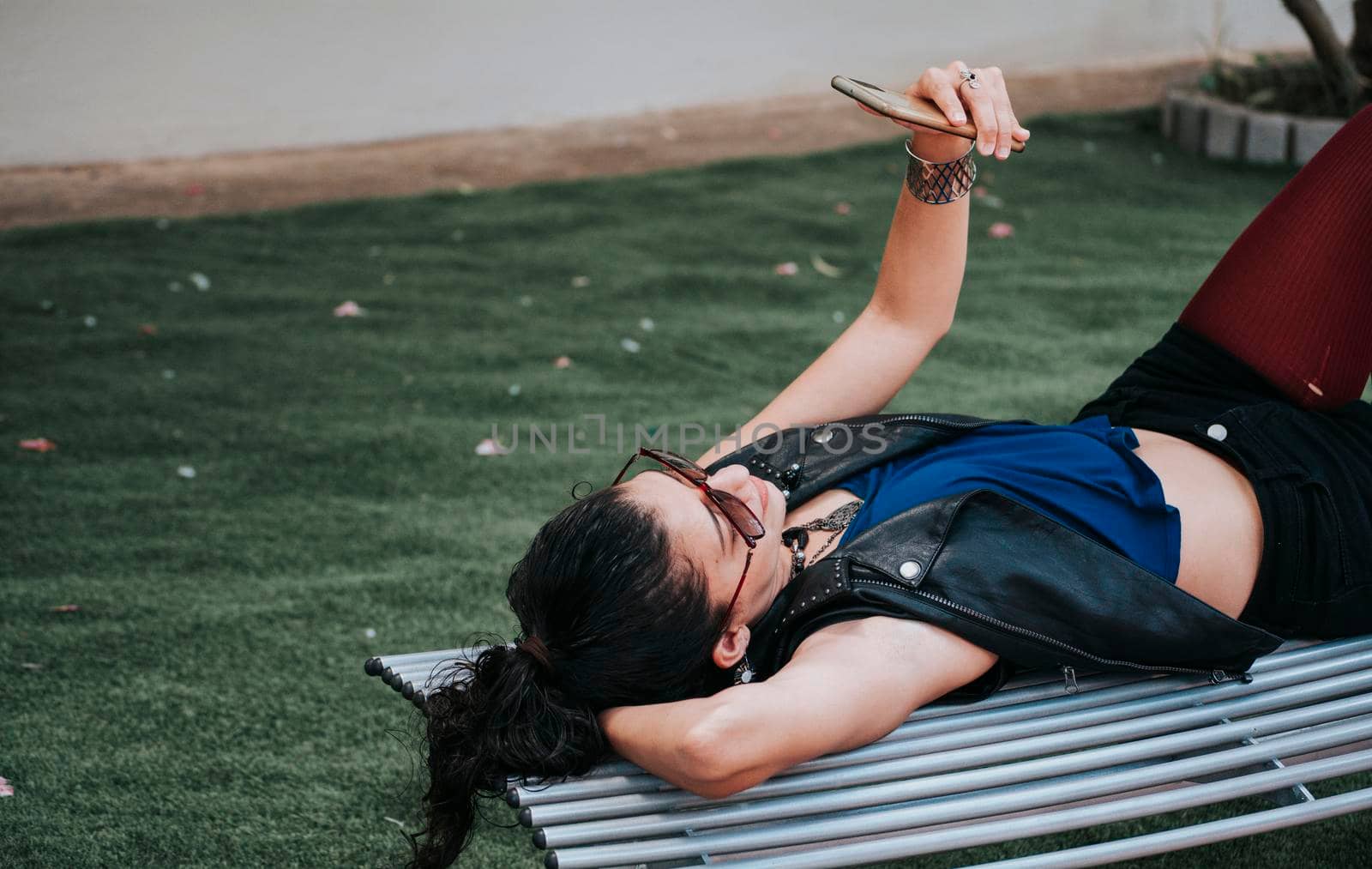 A girl lying on a bench with her cell phone, A woman lying on a bench with her cell phone, Girl lying down texting on her cell phone