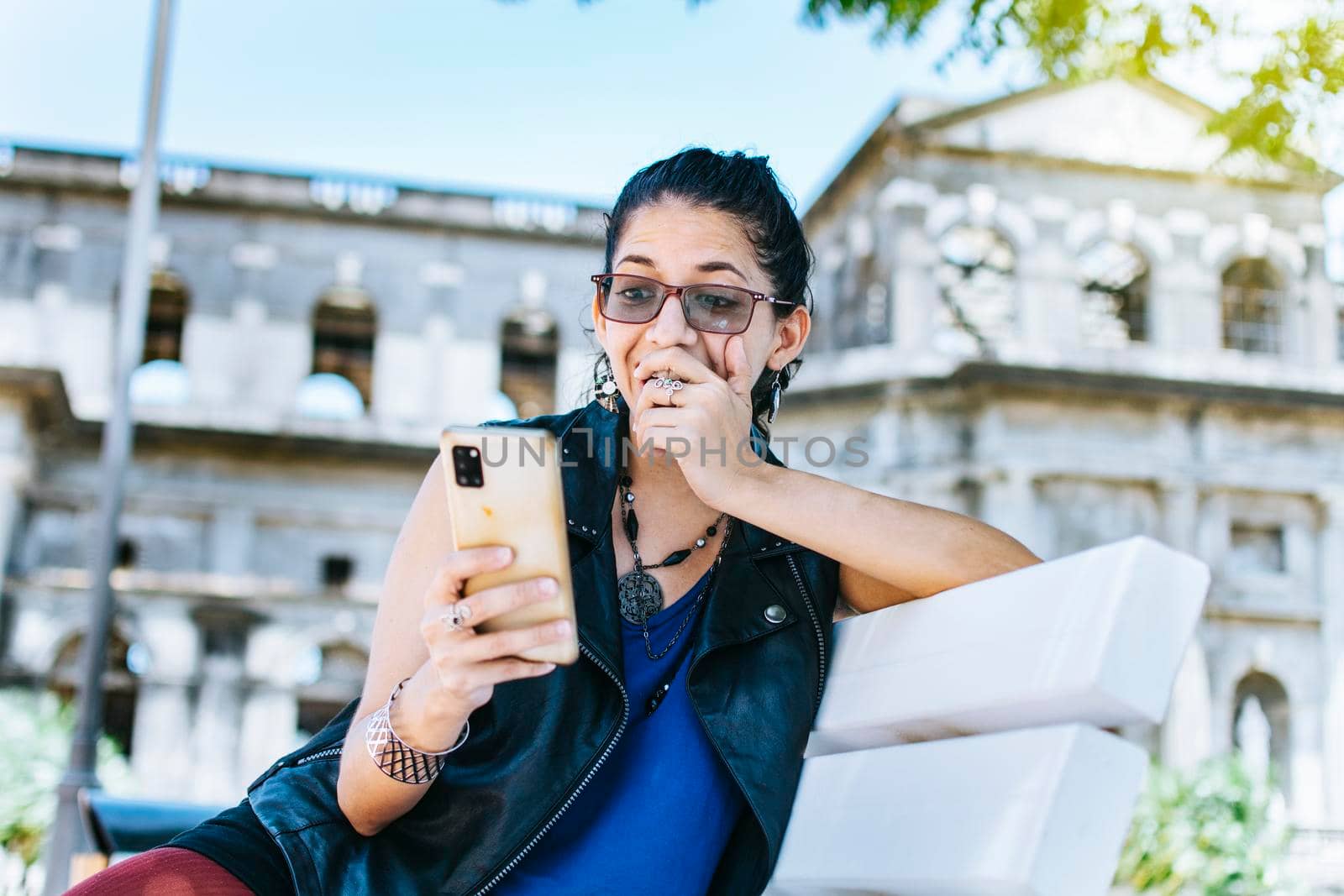 An attractive girl sitting on the cell phone smiling, Girl sitting on a bench texting on her cell phone, Urban style girl sitting on a bench with her cell phone