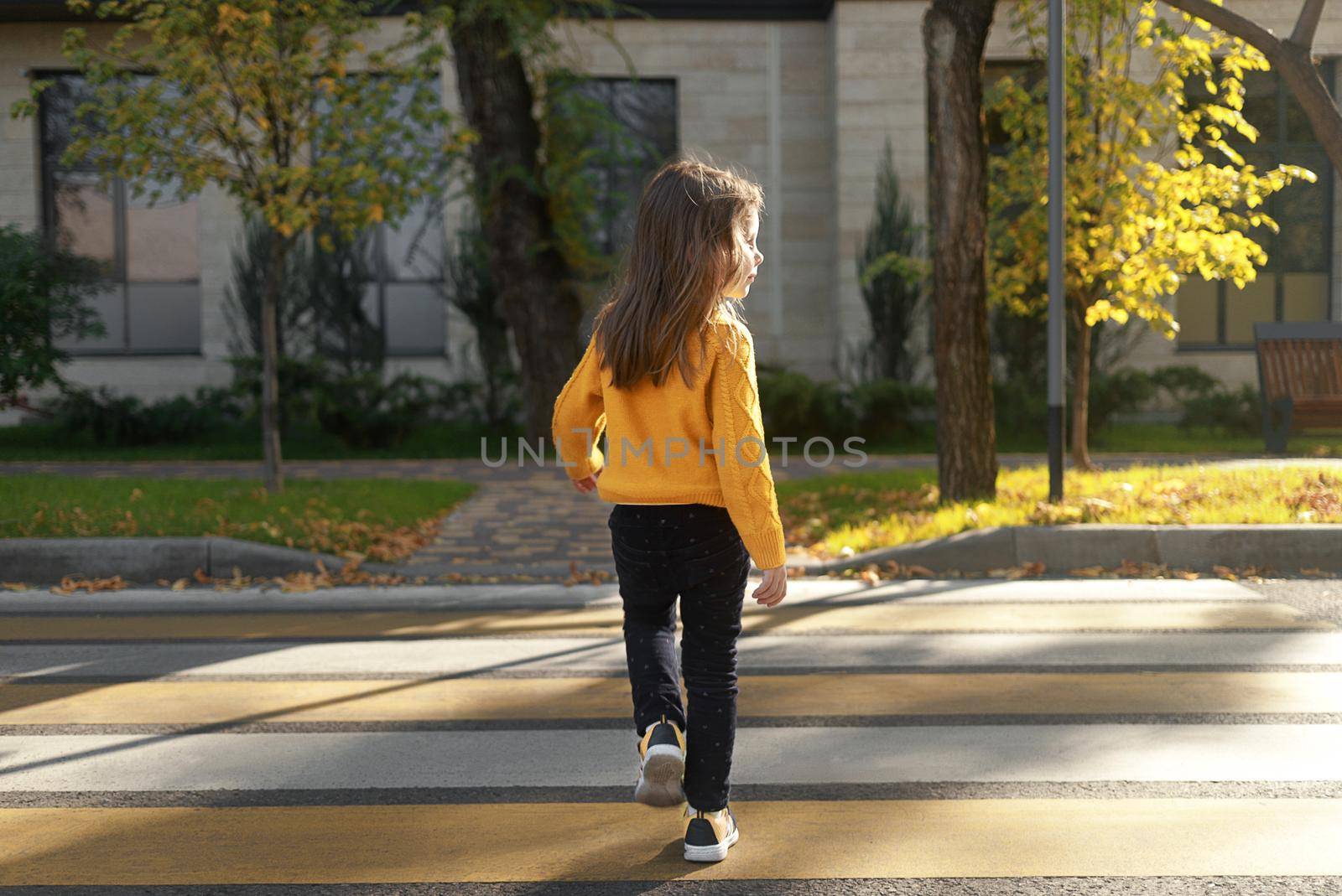 A little girl crosses the road on a zebra crossing, looks around.
