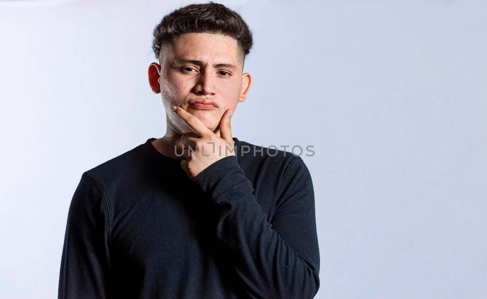 young man wondering with his hand on his chin on an isolated background, a guy thinking with his hand on his chin.