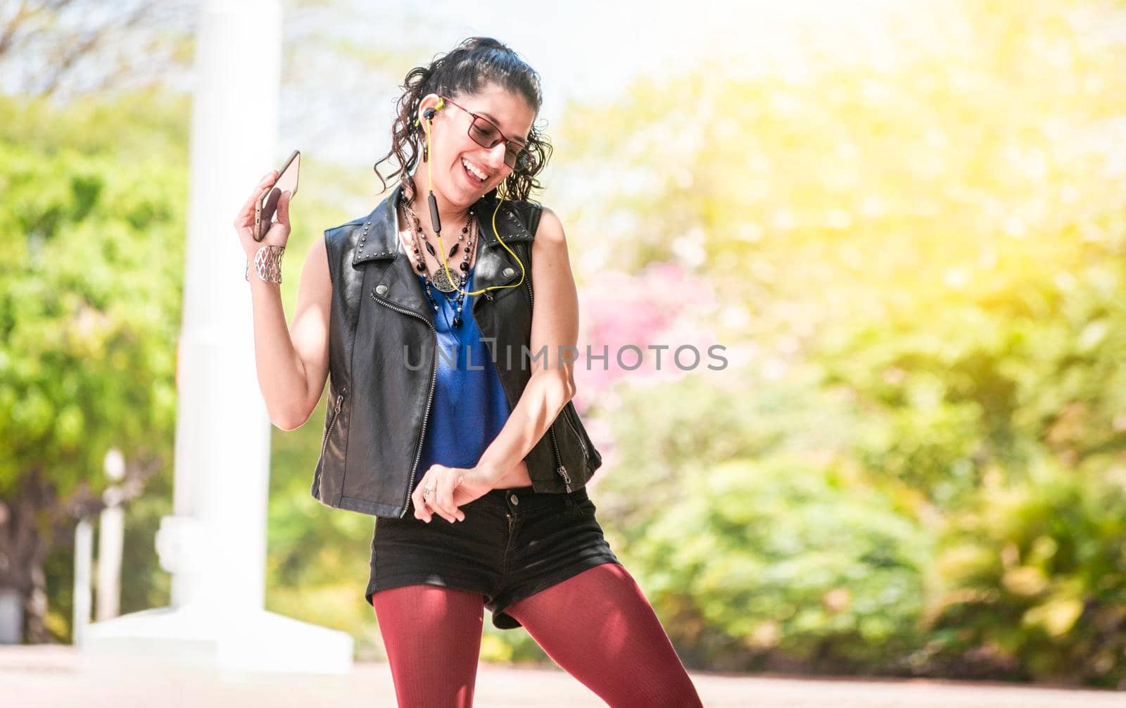 Latin girl listening to music outside, Urban girl enjoying music with headphones, Happy woman listening to music outside by isaiphoto