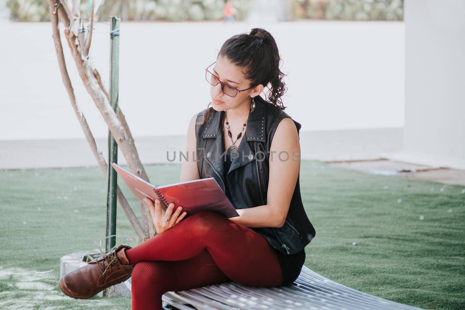 A student girl reading a book, urban girl sitting on a bench reading a book, Latin girl reading a book outside  by isaiphoto