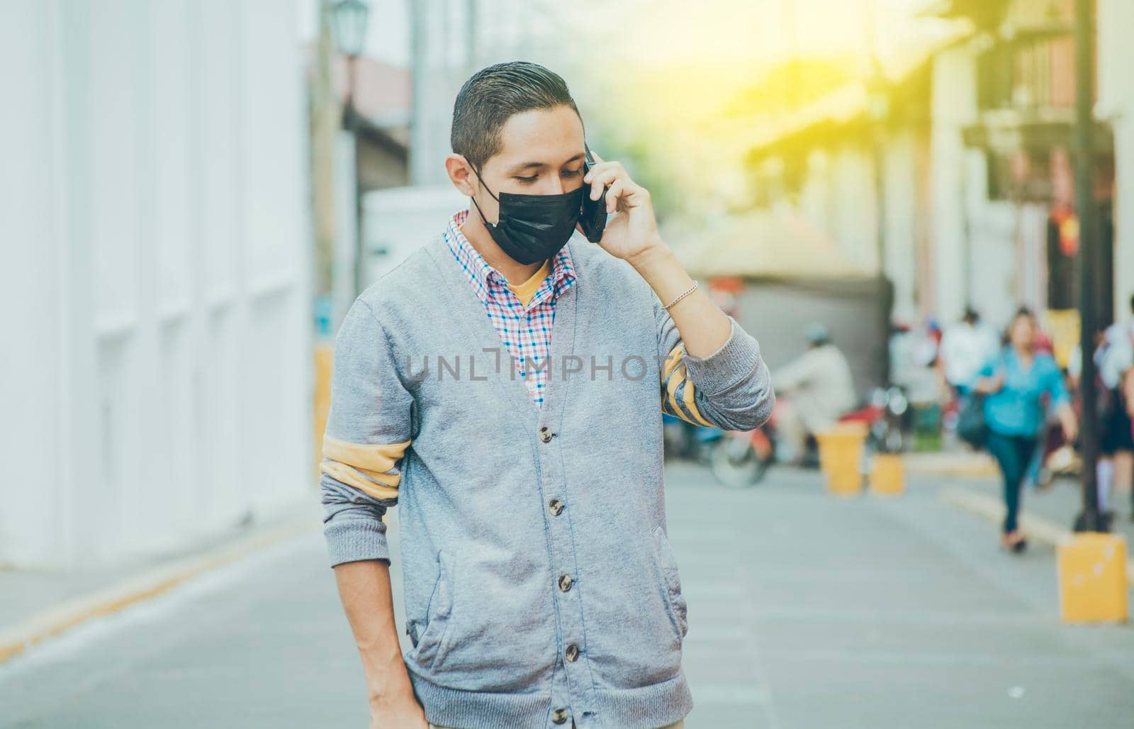 Man with surgical mask calling on the phone, latin man with mask calling on the phone in the street, man in mask calling on the phone in the street by isaiphoto