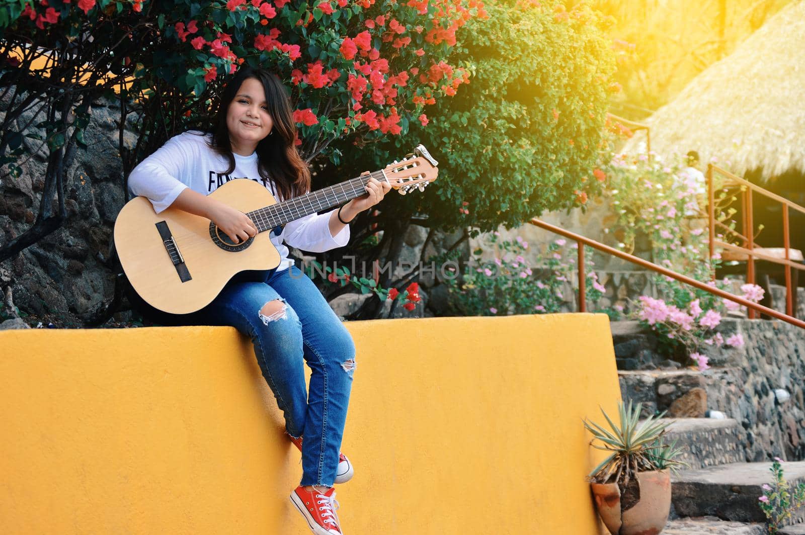 Pretty smiling girl sitting playing guitar outdoors, Portrait of smiling girl playing guitar, Lifestyle of girl playing guitar outdoors
