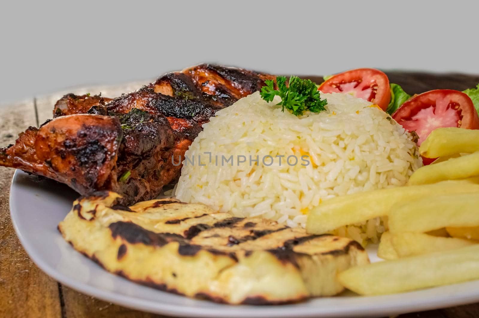 Pork rib with rice, fried cheese and tomato salad, Nicaraguan food served on wooden background, Plate of pork rib and rice served on wooden background