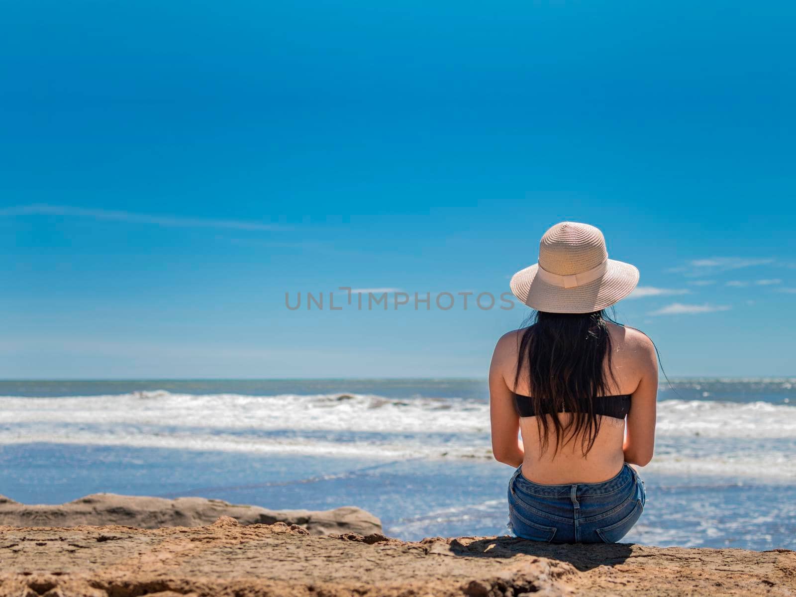woman in hat from back to the sea, girl in hat looking to the sea, vacation concept, rear view of a girl watching the sea