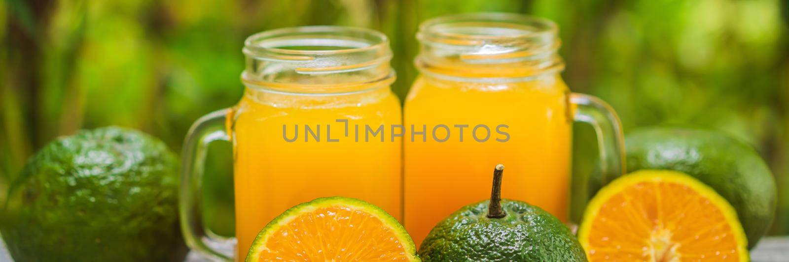 Orange juice and oranges with green peel on a wooden background. BANNER, LONG FORMAT