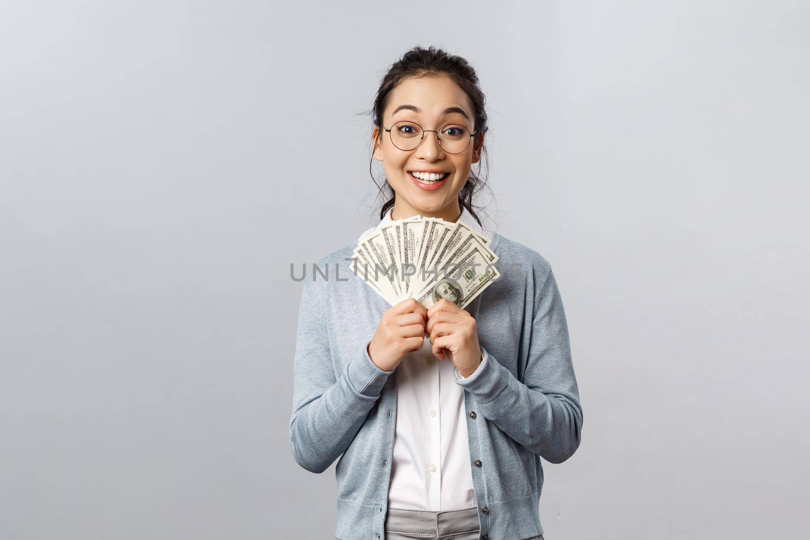 Business, finance and investment concept. Excited happy and upbeat smiling asian female winning prize in lottery, receive award money, holding cash dollars and grinning emotional.