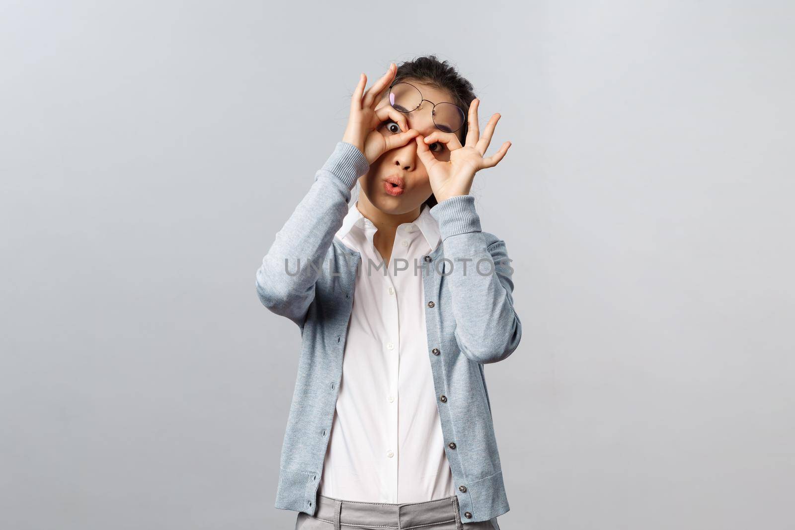 Lifestyle, people and emotions concept. Funny, playful silly asian girl fool around, playing with you, make glasses mask with fingers over eyse, peekabo at kid, staring camera joyful by Benzoix