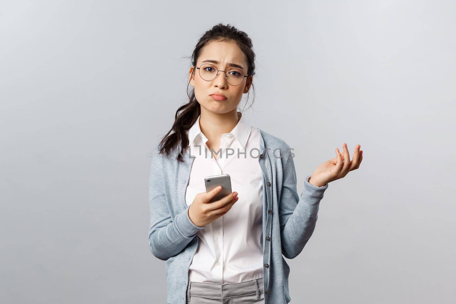 Office lifestyle, business and people concept. Gloomy indecisive and puzzled asian woman having proble, shrugging troubled and unsure, sighing, cant figure out how answer on message, use mobile phone.