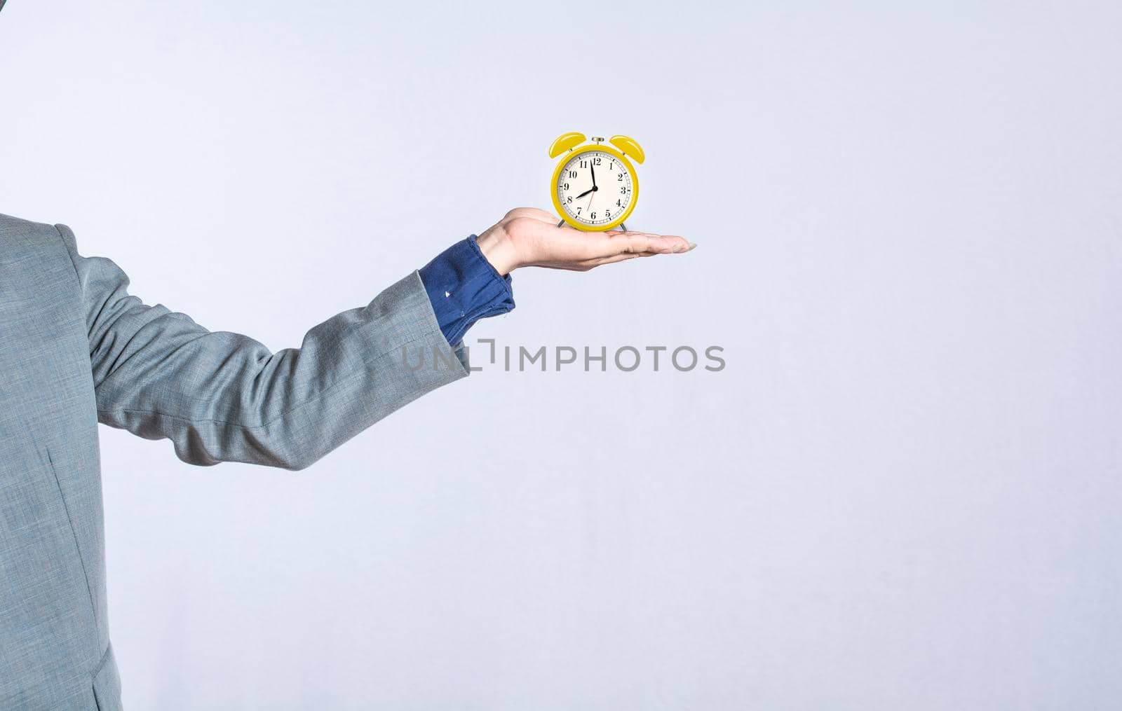A hand holding a table clock on isolated background, close up of a hand holding an alarm clock, businessman hand holding clock isolated by isaiphoto