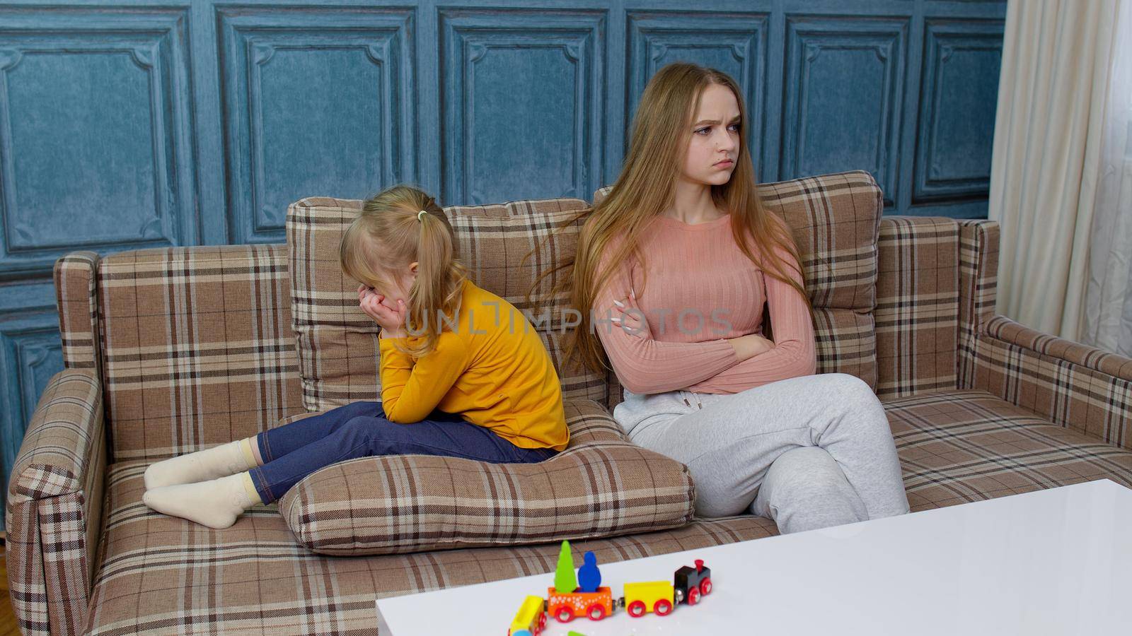 Unhappy stressed woman and angry little child sister ignoring each other sitting on couch after quarrel. Upset girl sibling avoid talk sitting turned back on sofa at home having argument with family