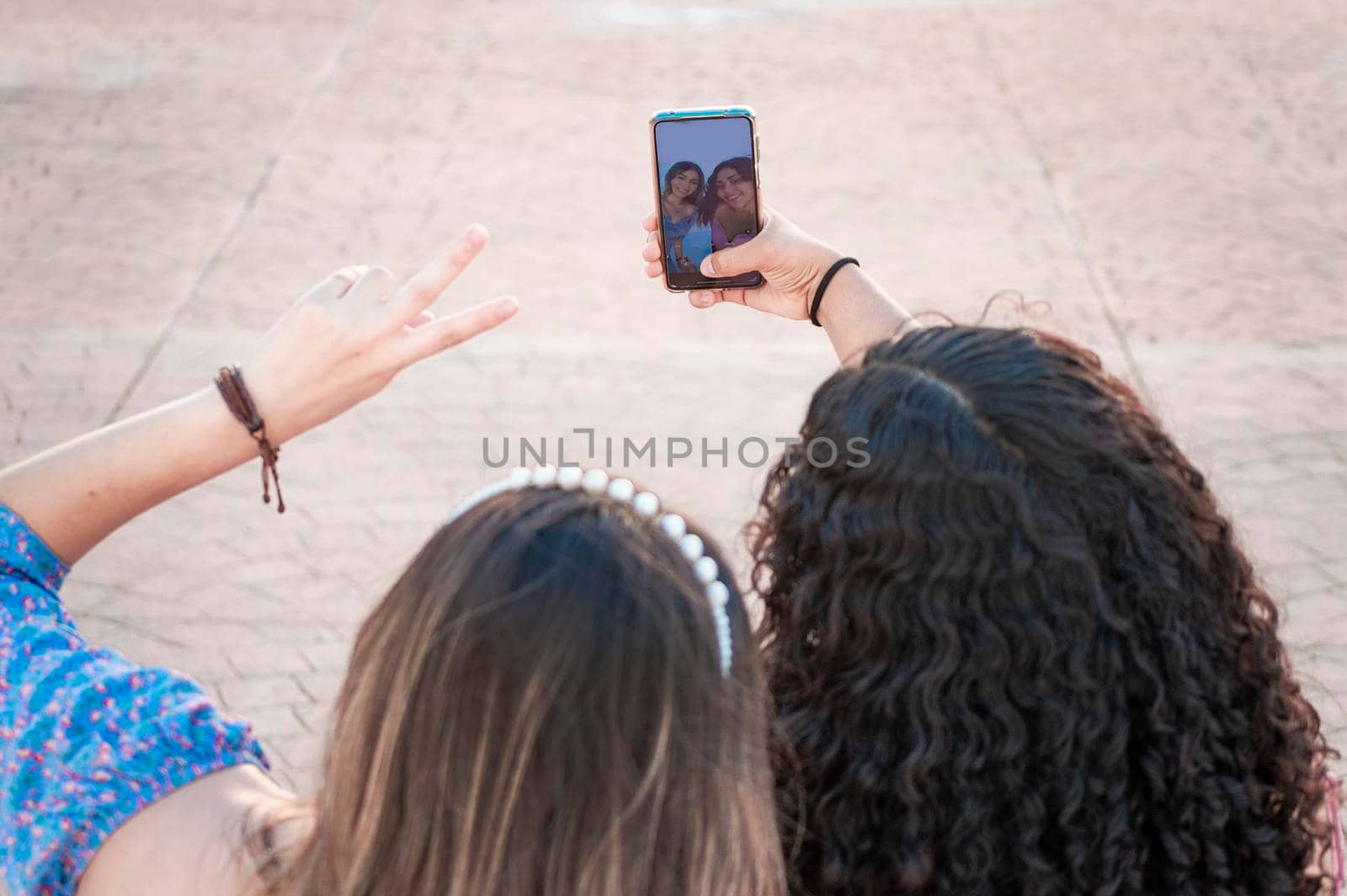Two pretty girls taking a selfie, two latin girls smiling and taking a selfie, female friendship concept by isaiphoto