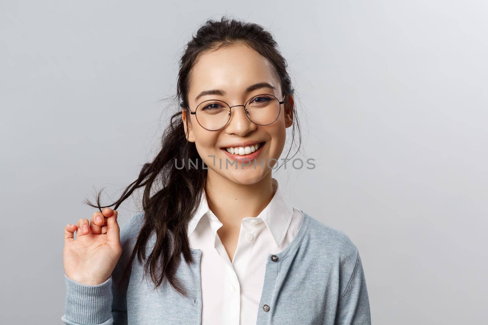 Close-up portrait of flirty, enthusiastic brunette asian female in glasses, beaming smile, roll strand of hair between fingers as coquettish talking to person she likes, standing grey background by Benzoix