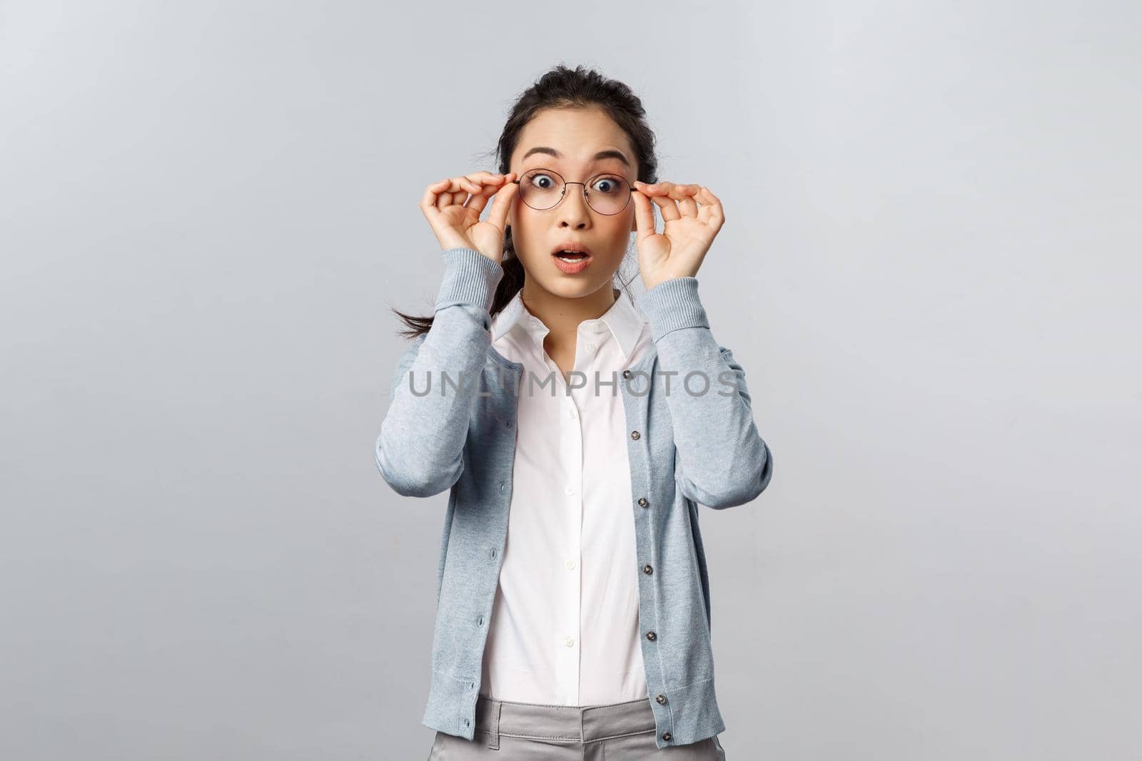 Shocked, startled attractive asian woman staring in awe, drop jaw and gasping, put on glasses to see fascinating piece of art at exhibition, staring impressed and wondered, grey background by Benzoix