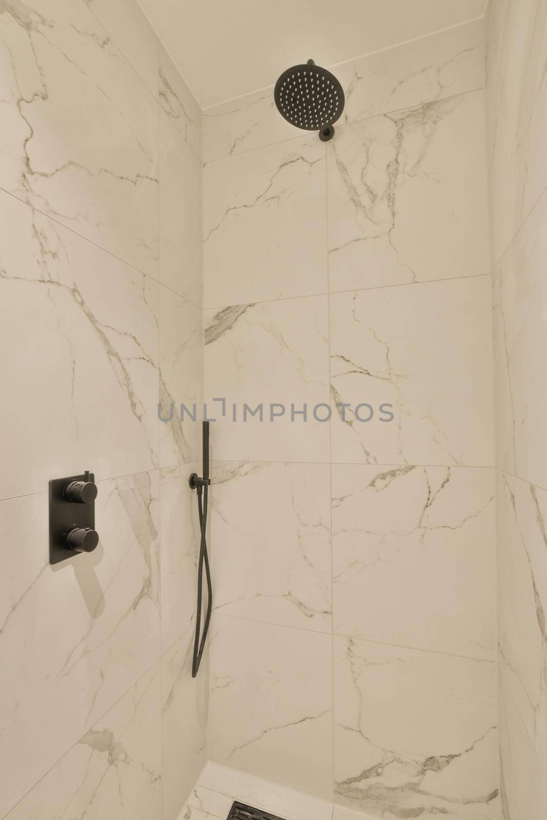 Shower faucets attached to tiled wall near glass partition and ornamental curtail in washroom at home