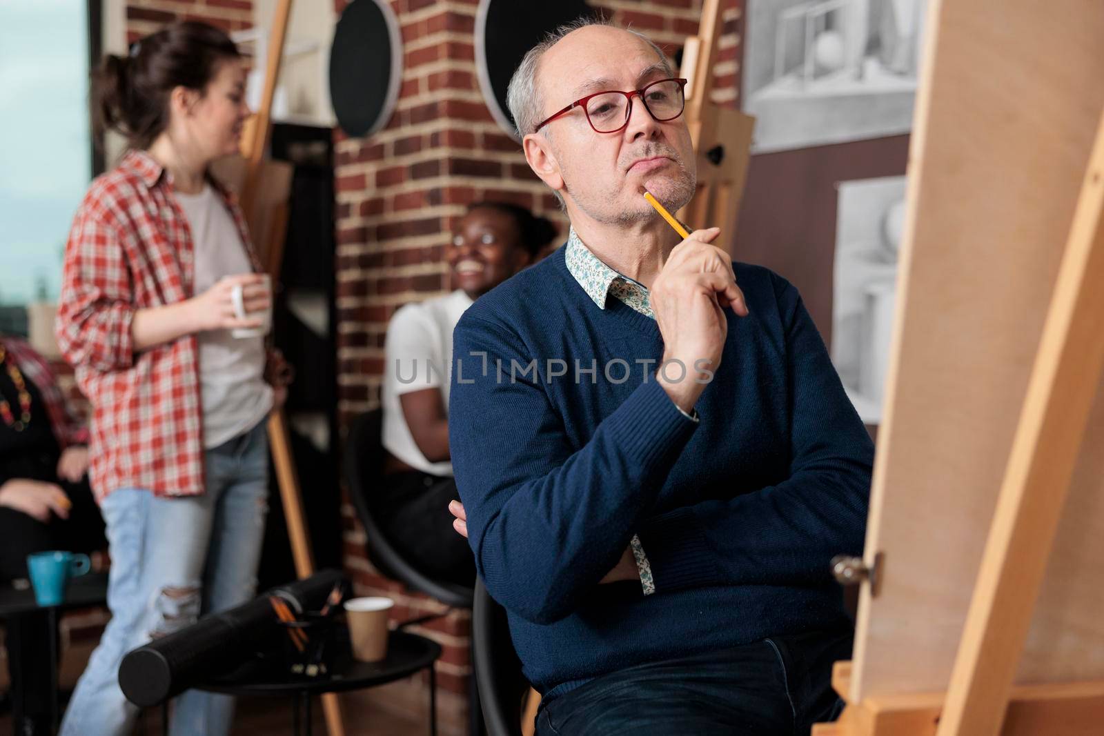 Portrait of elderly student drawing vase on white canvas sketching model using graphic pencil in creativity studio. Diverse team attenting art course developing new artistic skill for personal growth