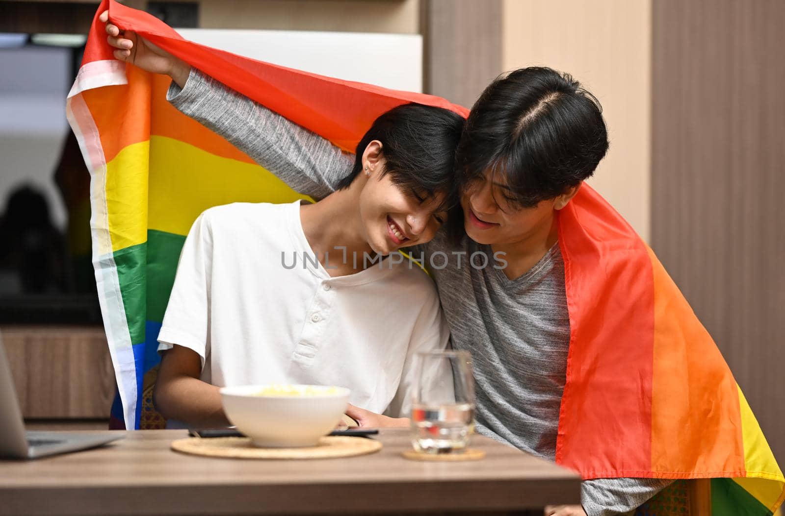 Young gay couple under LGBTQ pride flag. Concept of sexual freedom and equal rights for LGBT community.