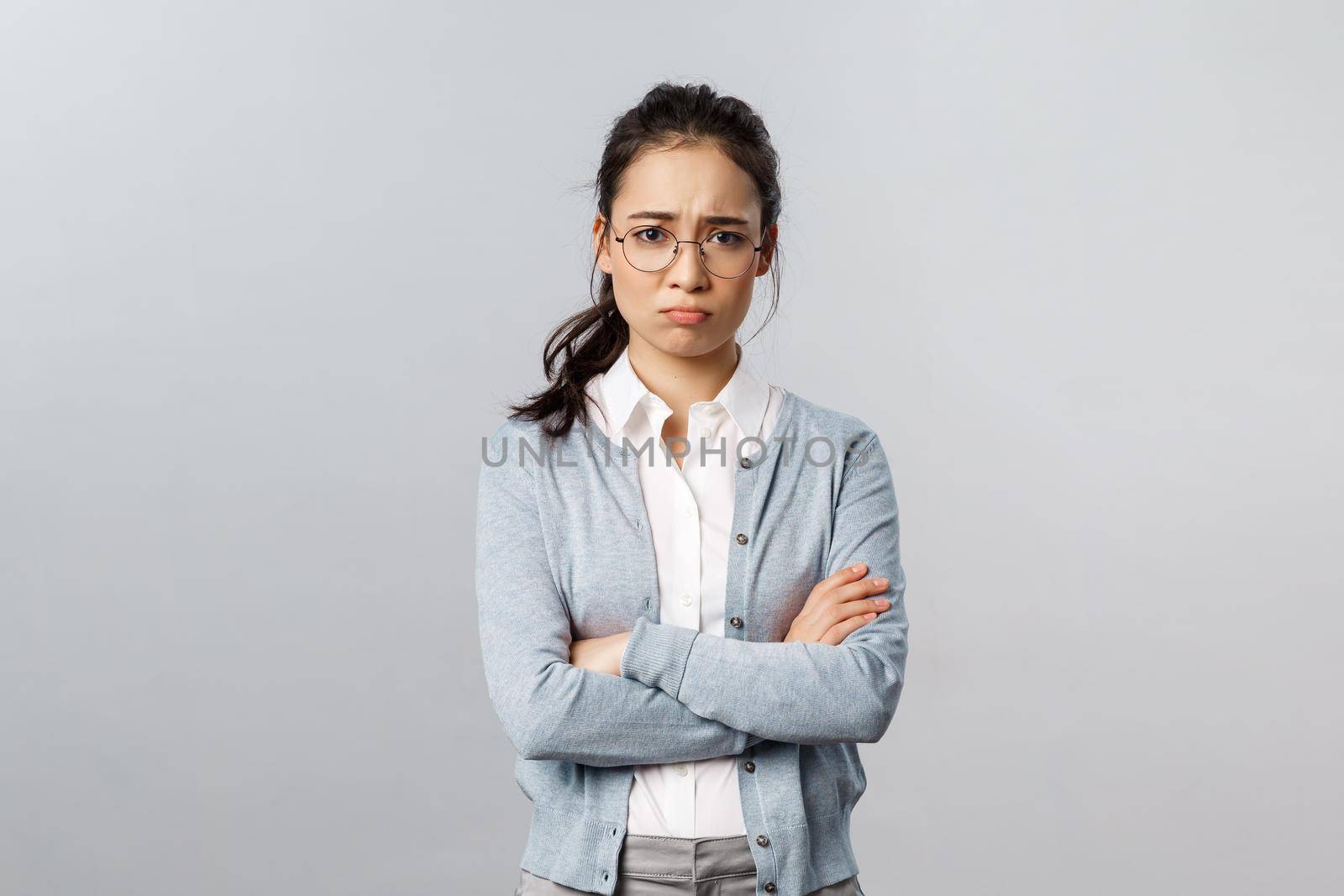 Portrait of offended insecure and timid cute asian girl complaining on cruel customer being rude to her, cross hands over chest defensive and upset, frowning gloomy, feel upset grey background.