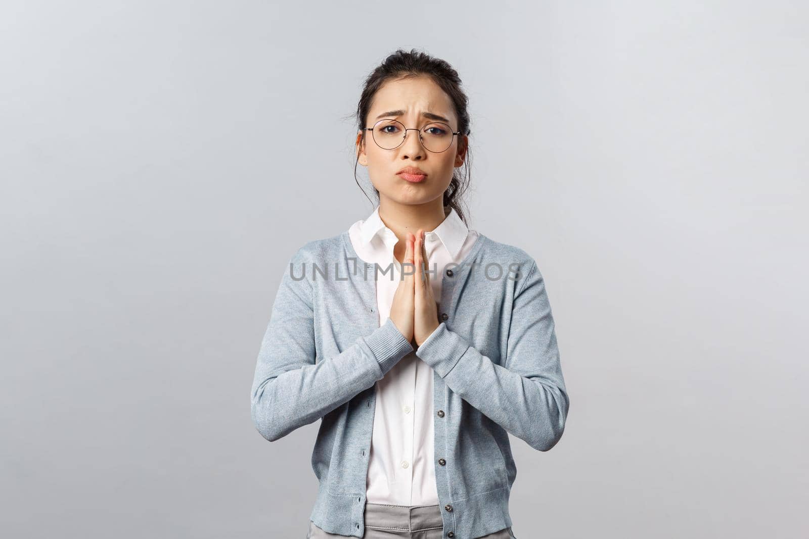 Emotions, people and lifestyle concept. Pretty please help me out. Portrait of cute, adorable asian woman asking coworker cover her, hold hands in pray, pleading for favour, standing grey background.
