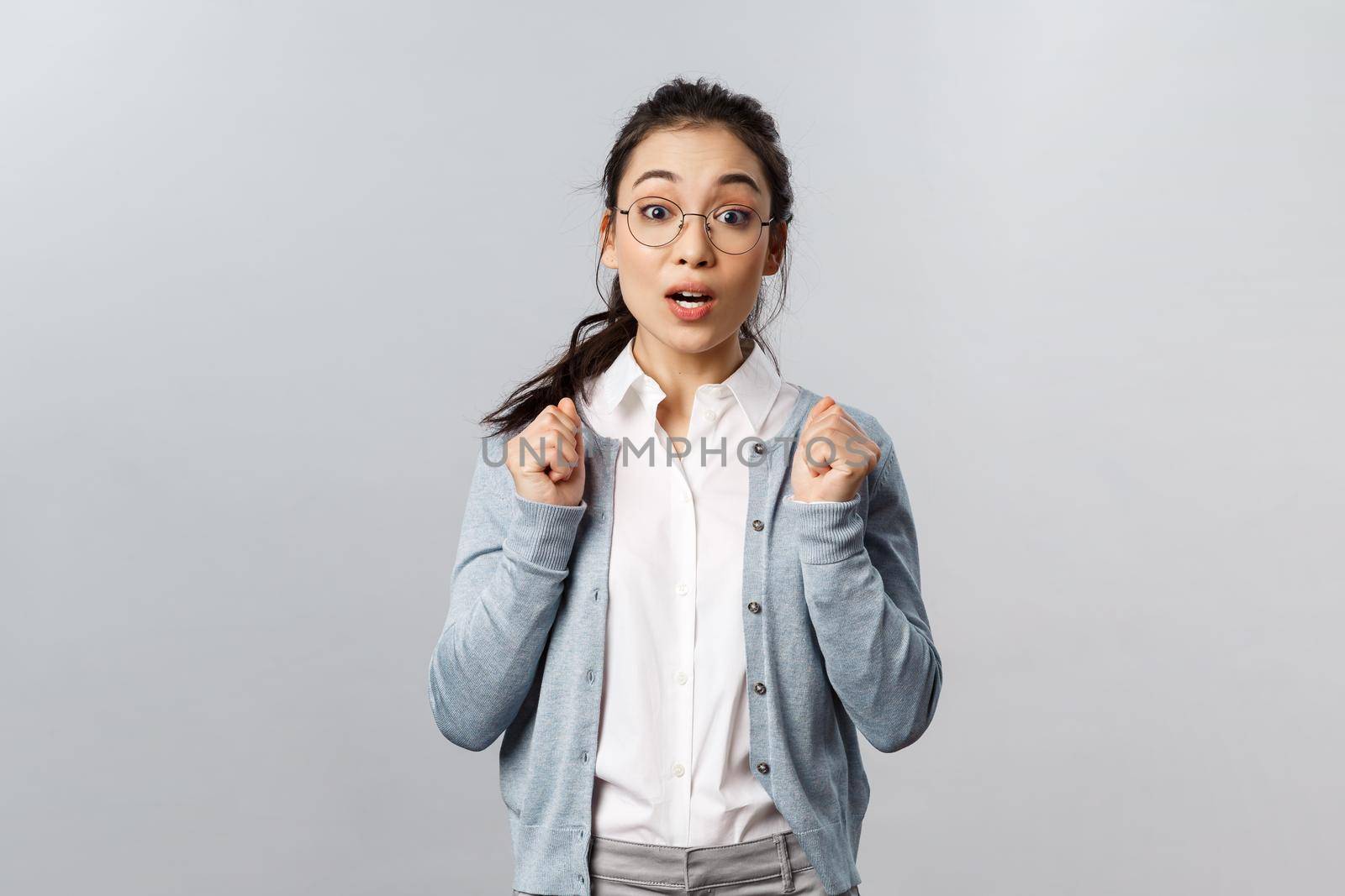 Portrait of excited and tempting cute asian girl in glasses, awaiting with thrill and interest for new season of favorite tv show coming up, looking ancitipation and amusement, stand grey background.