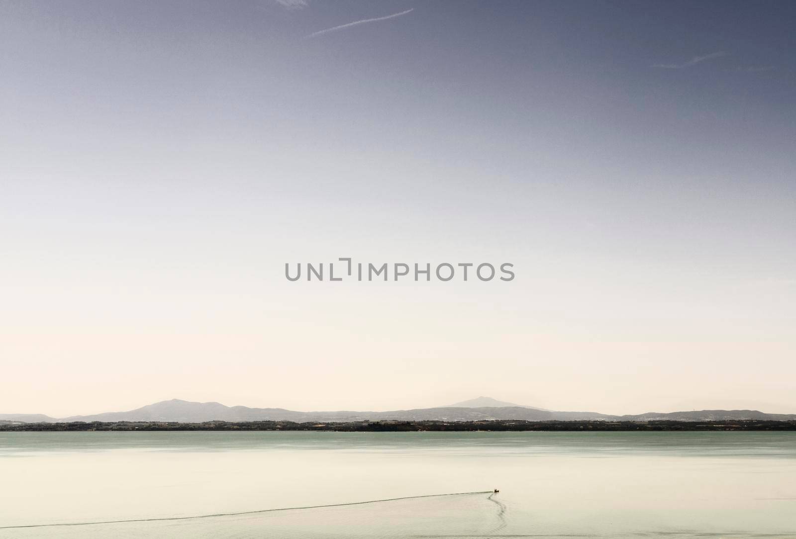 One sail boat in the calm waters of Lake Trasimeno , Italy , in the foreground rocks on the water