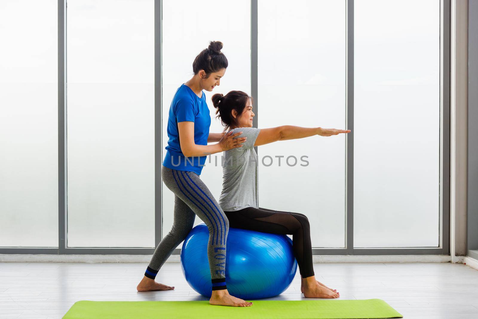 adult and young woman in sportswear doing aerobics yoga exercise with sitting on fitness ball by Sorapop