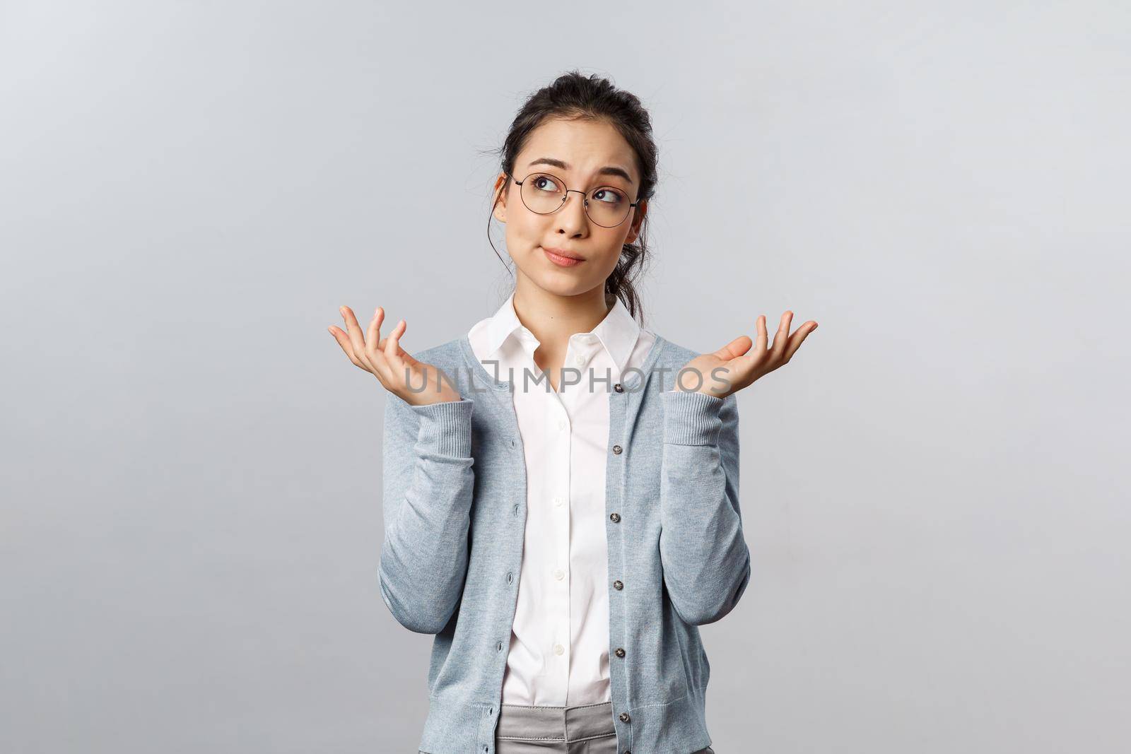 Lifestyle, people and emotions concept. Indecisive clueless asian woman in glasses, thinking, cant make-up idea, shrugging with hands spread sideways puzzled, dont know have no answer.