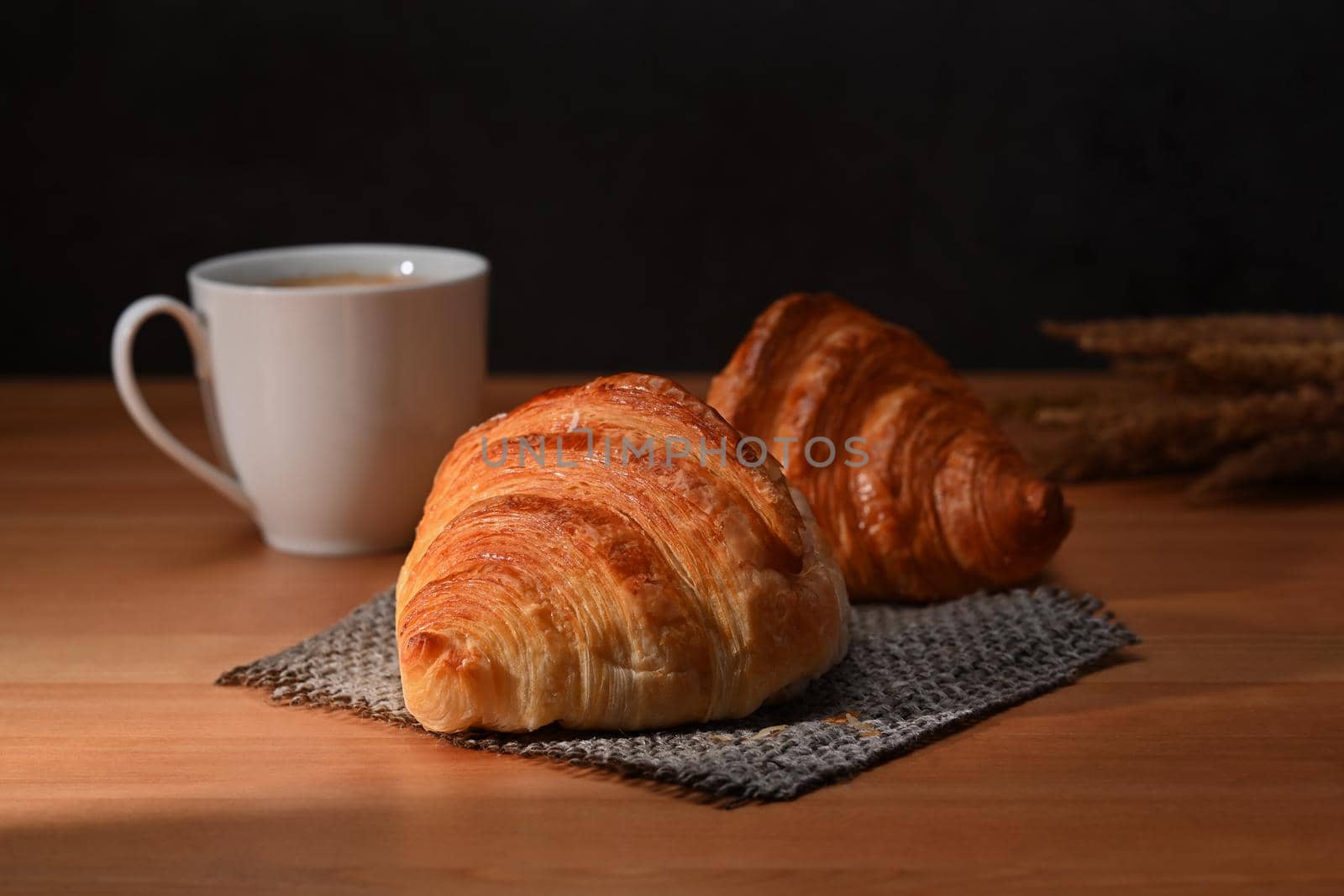 Delicious, fresh croissants and coffee cup on wooden table for homemade breakfast.