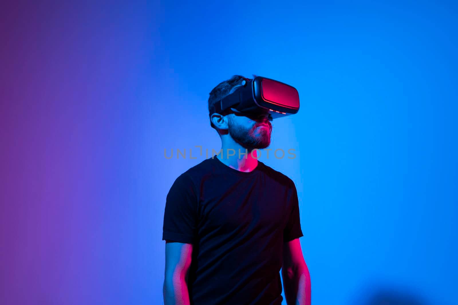 Young bearded man in virtual reality helmet plays online game in metaverse. Game simulates behavior in fictional world, gadgets and virtual reality addiction. Future technology concept. by vovsht