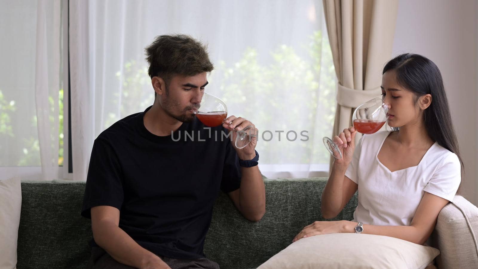 Happy couple resting on sofa and drinking wine. Leisure and celebration concept.