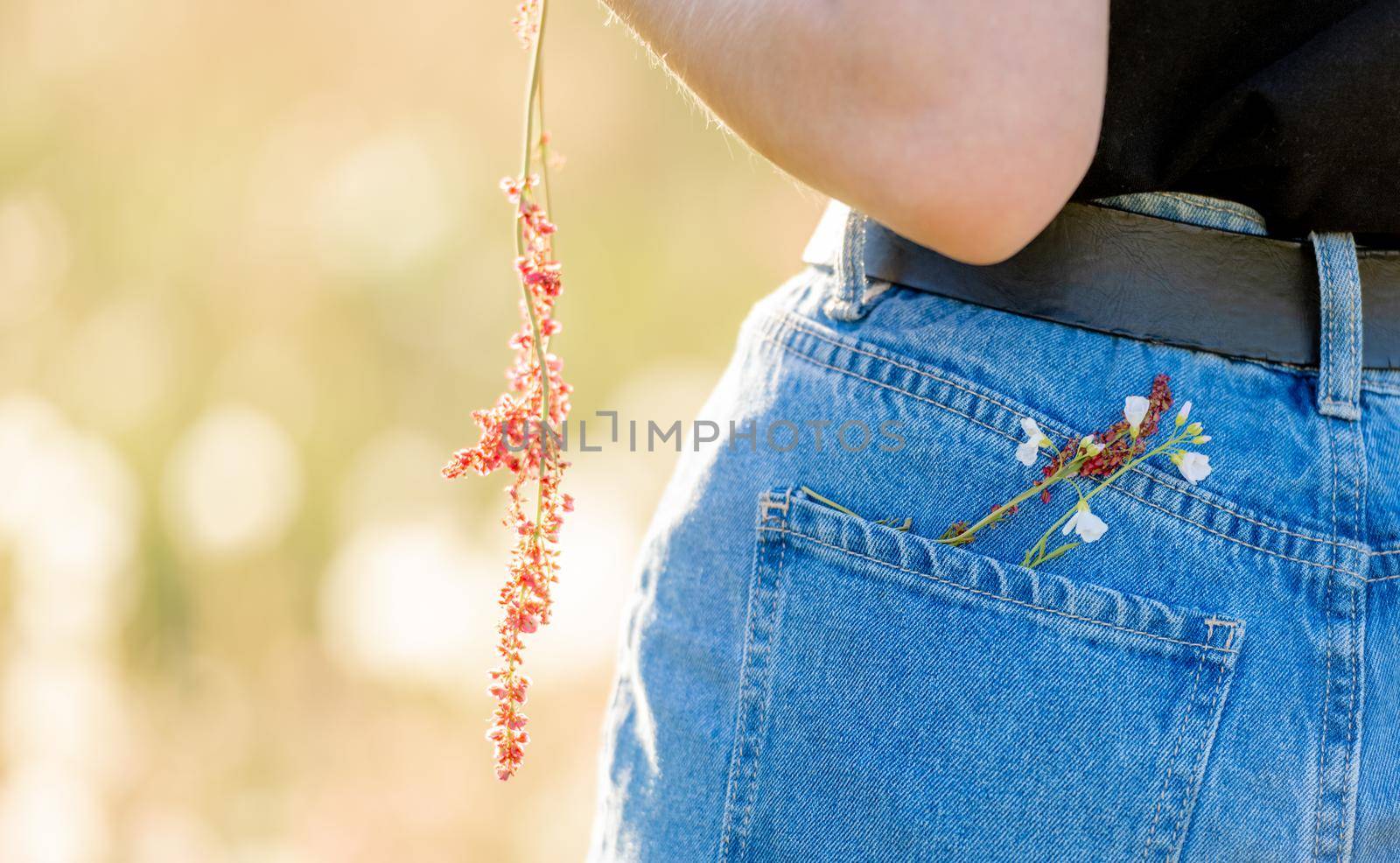 Girl wearing jeans denim with flowers closeup details. Female person in cotton pants in field