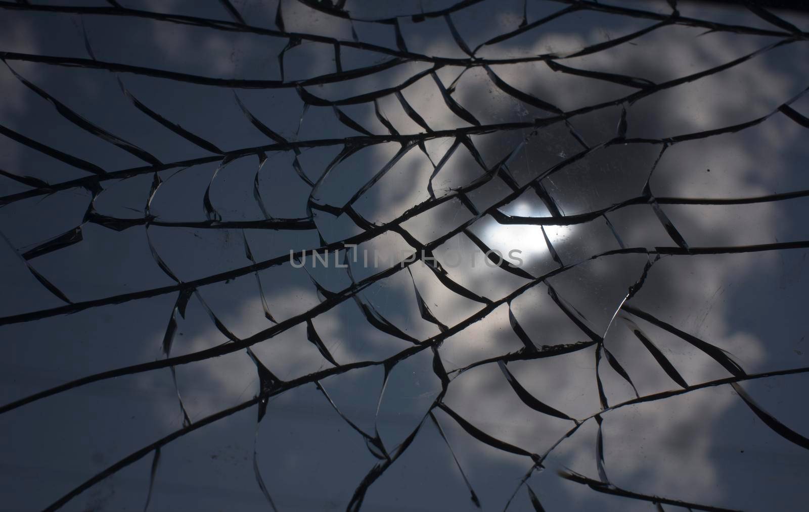 Broken glass with cracks on blue sky background. Close up view of broken glass texture