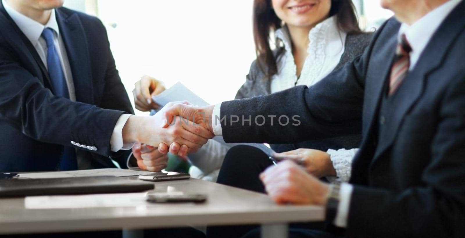 Mature businessman shaking hands to seal a deal with his partner and colleagues in a modern office