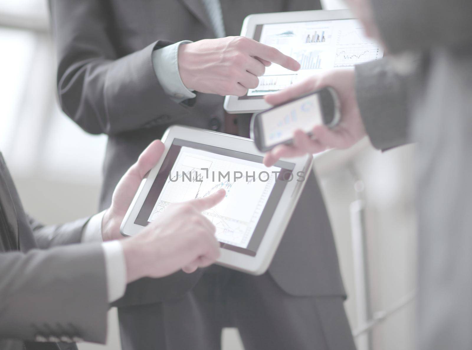Businessmen at meeting presenting charts on smartphone, tablet.
