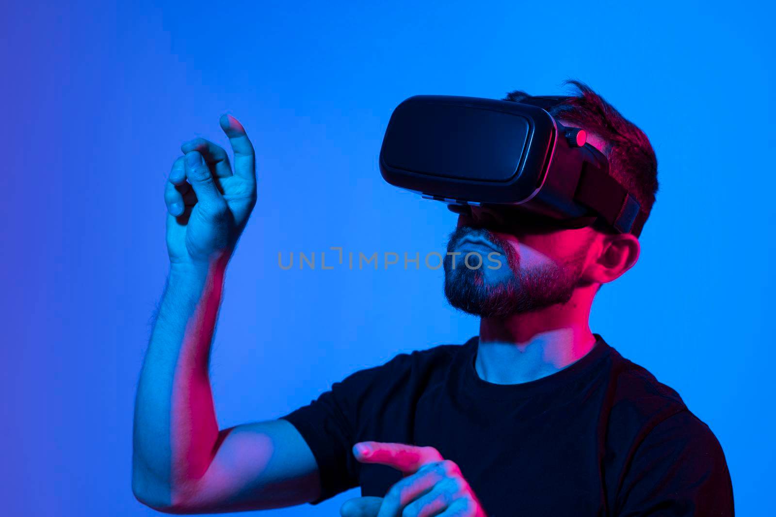 Man in virtual 3d glasses working on a project in a studio in neon light. Man playing video games with a friends at home using vr goggles. by vovsht