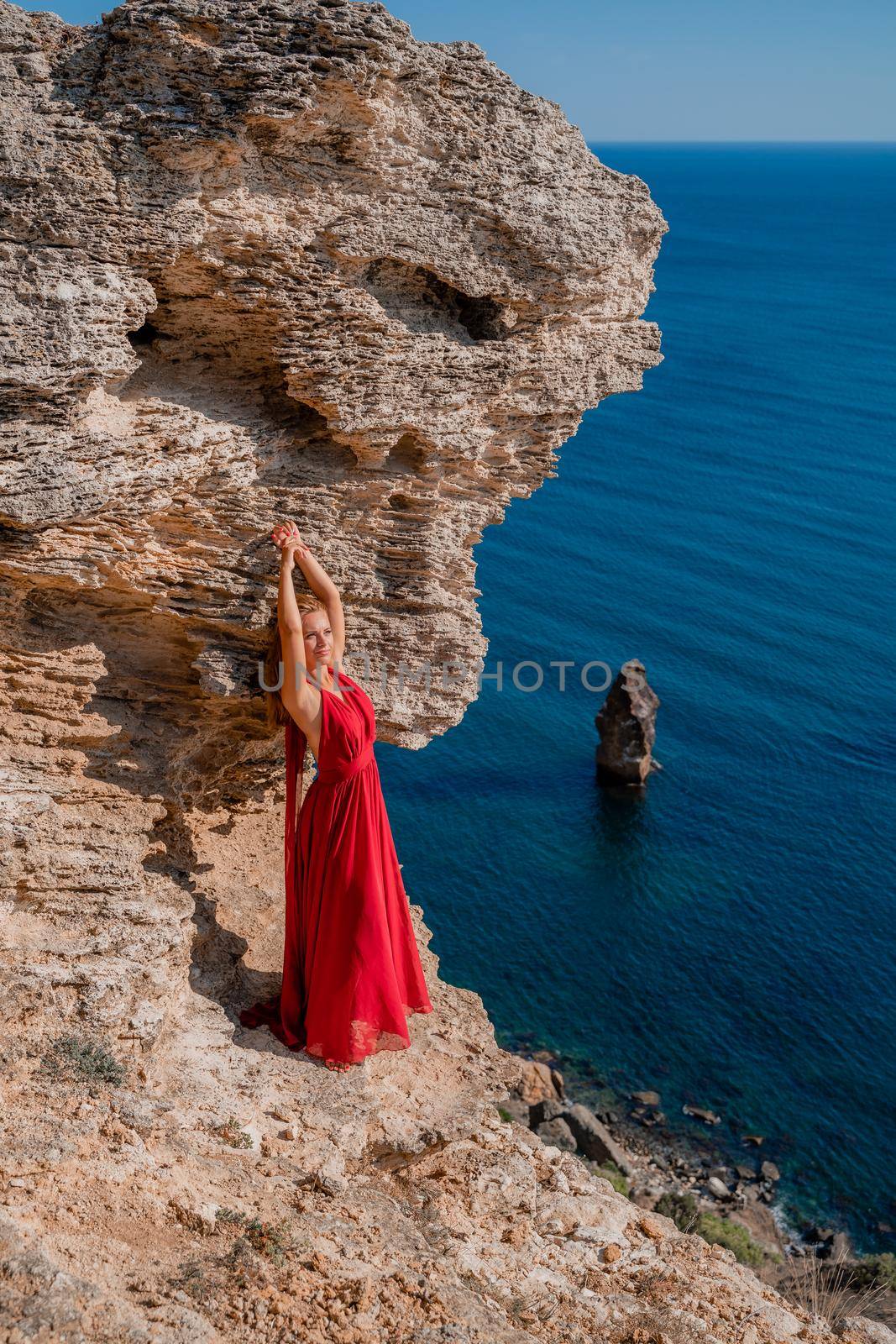 A woman in a red flying dress fluttering in the wind, against the backdrop of the sea